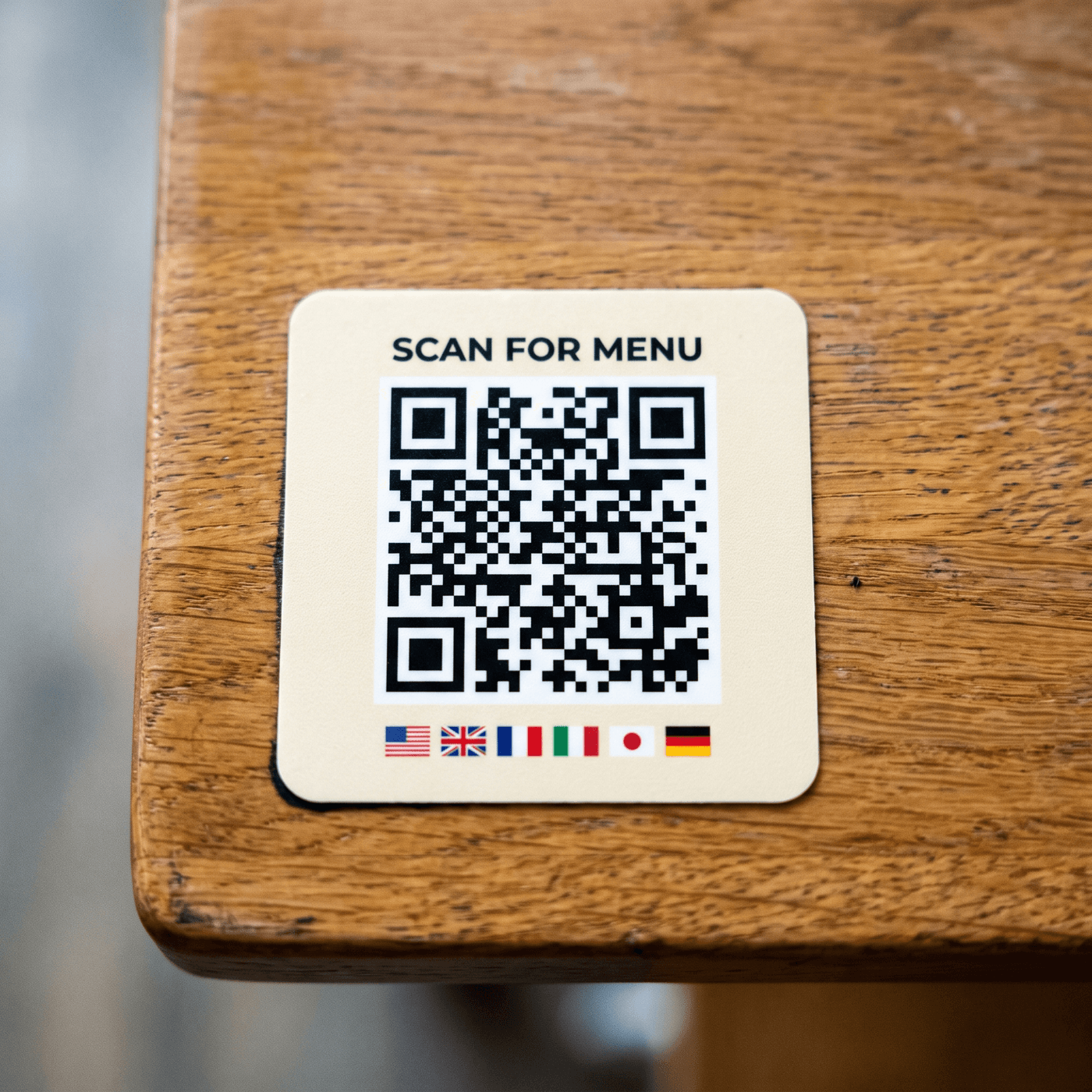 Table sticker or tent card with the QR code, on a real table. Cutlery and a glass in frame, warm restaurant light. 840×640.